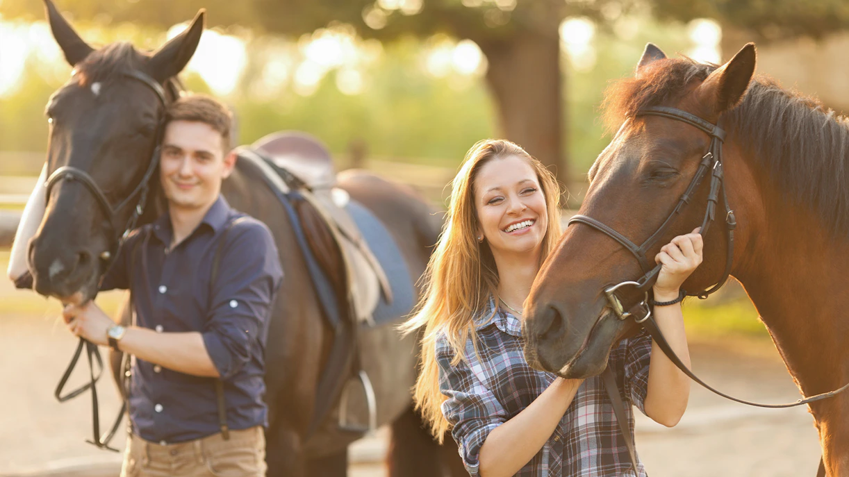 Couple enjoying horse riding experience in a sunny outdoor setting.
