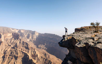 Tourist standing on cliff edge overlooking deep canyon in Jebel Akhdar, Oman.