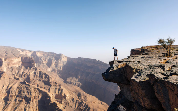 Tourist standing on cliff edge overlooking deep canyon in Jebel Akhdar, Oman.