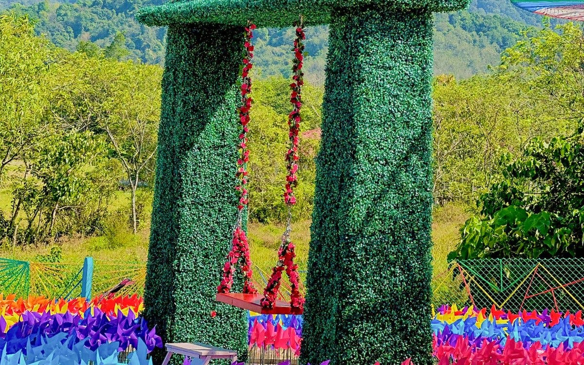 Swing adorned with red flowers at De Windmill Selfie Park, surrounded by colorful pinwheels.