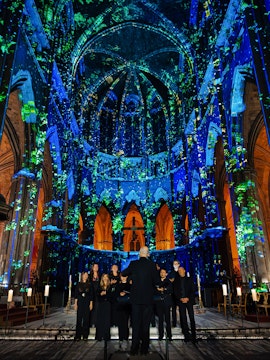 Choir performing under illuminated arches at Manchester Cathedral during LUMINISCENCE 360° show.