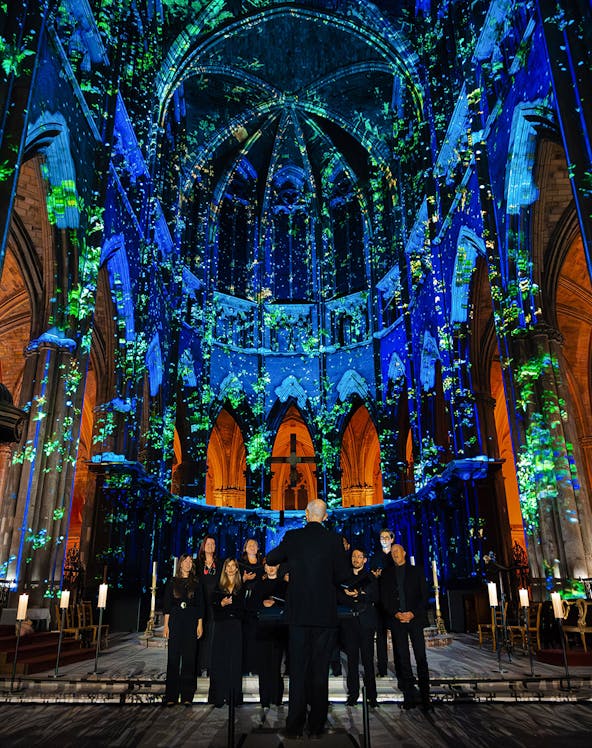 Choir performing under illuminated arches at Manchester Cathedral during LUMINISCENCE 360° show.