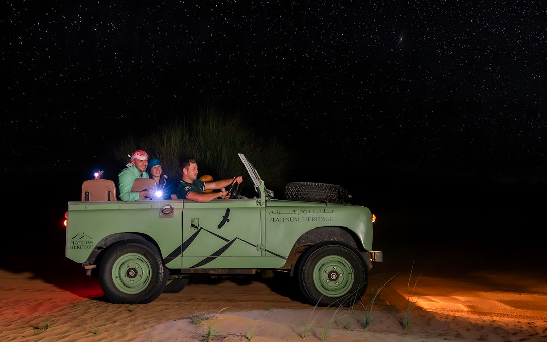 Vintage jeep on a desert night safari under a starry sky.