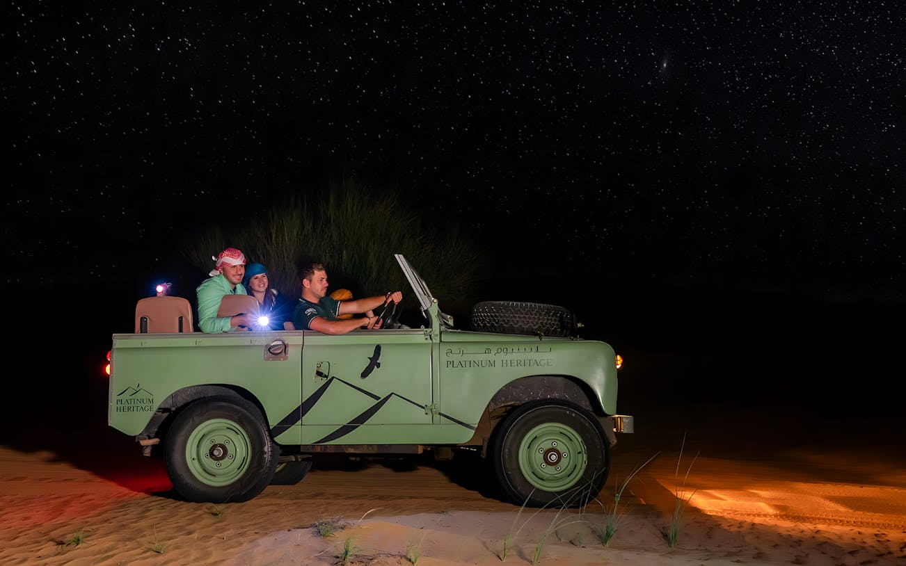 Vintage jeep on a desert night safari under a starry sky.