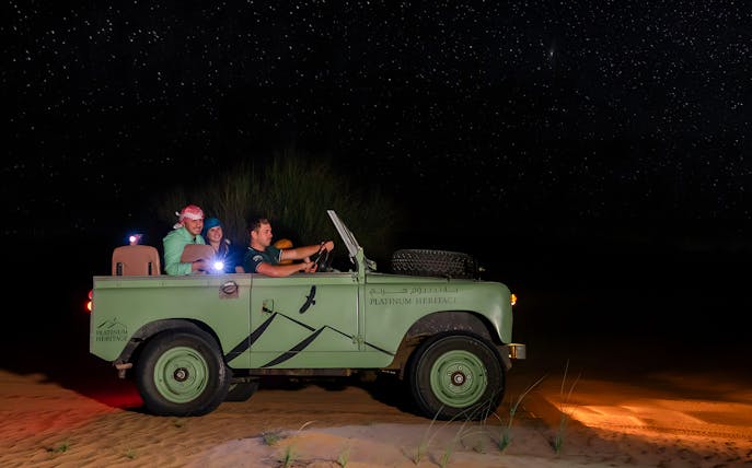 Vintage jeep on a desert night safari under a starry sky.