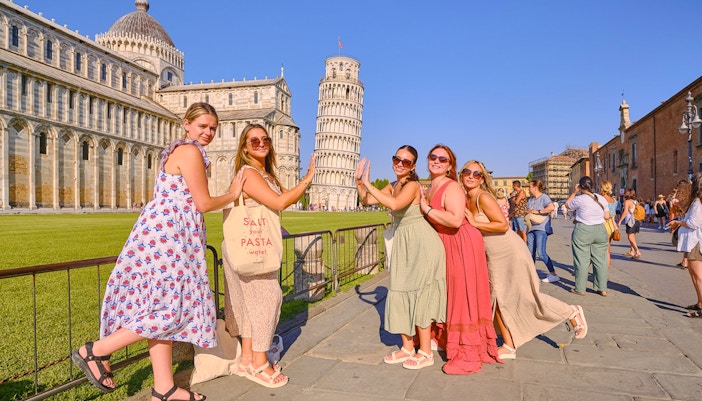 Women posing playfully with the Leaning Tower of Pisa in Italy.
