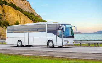 Bus on coastal road for Cape Sounio and Poseidon Temple trip transfers.