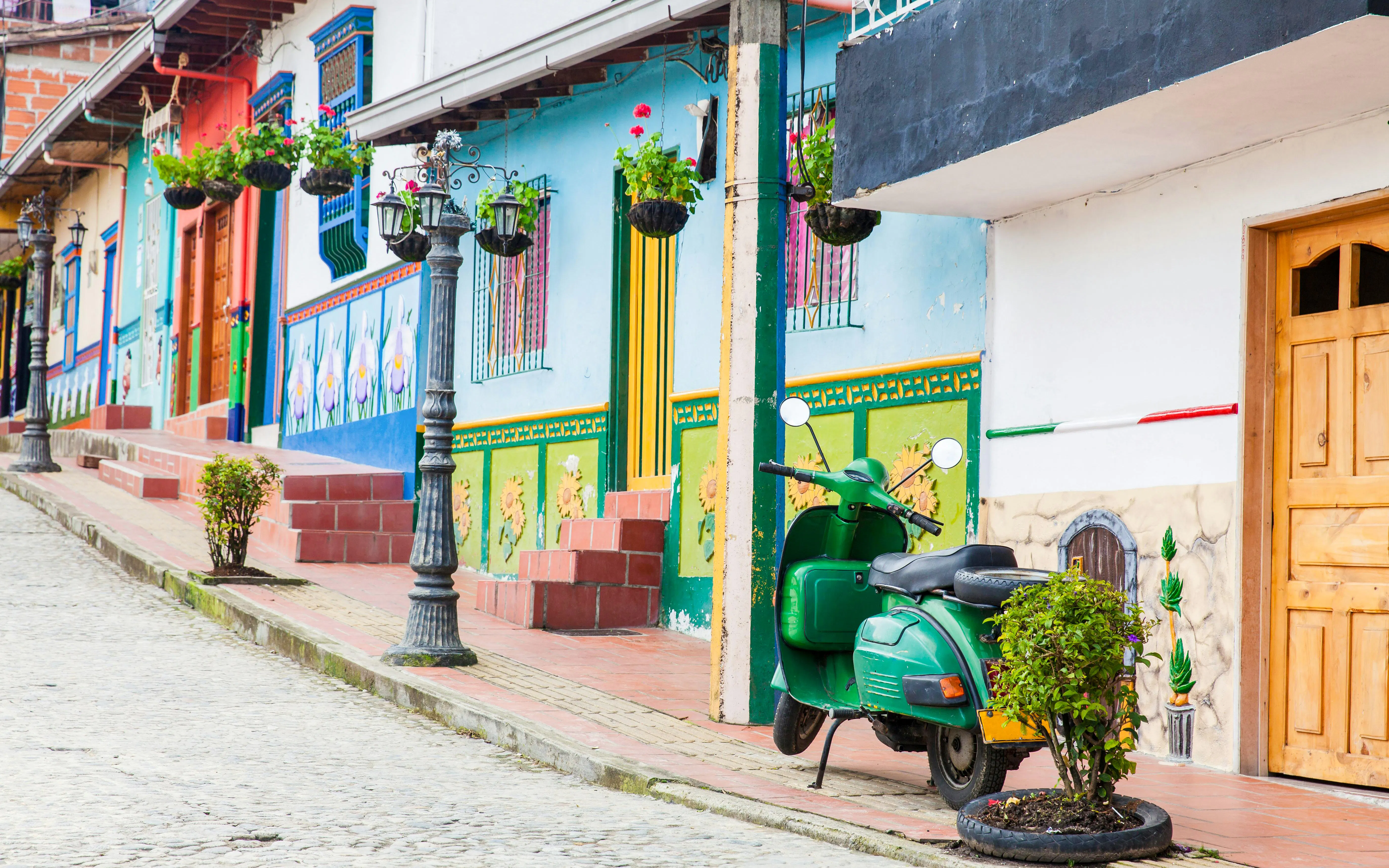 Green motorcycle parked by colorful murals in Guatapé, Antioquia, Colombia.