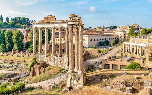 Ancient ruins and columns on Palatine Hill, Rome, with cityscape in the background.