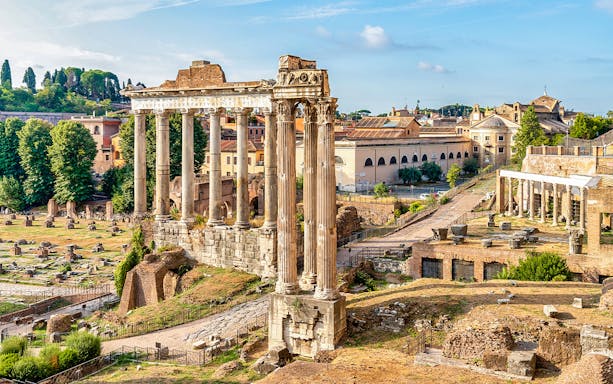 Ancient ruins and columns on Palatine Hill, Rome, with cityscape in the background.