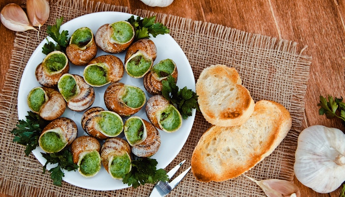 Escargot with garlic butter on a plate, served with toasted bread and parsley.