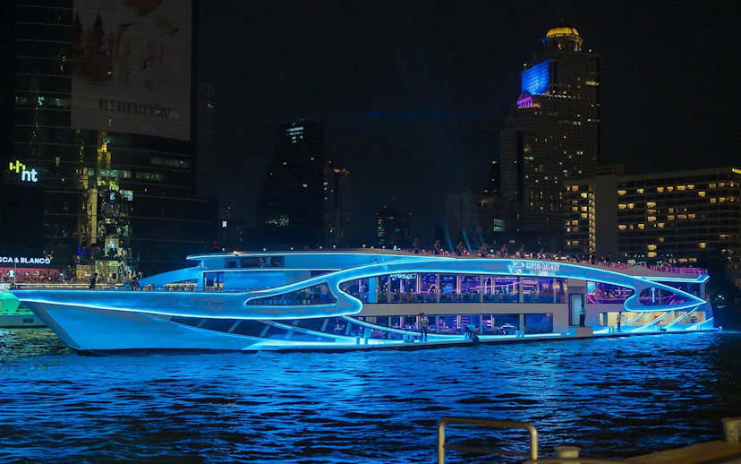 Luxury dinner cruise on Chao Phraya River, Bangkok, with city skyline at night.