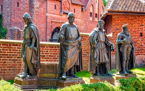 Statues of knights in front of Malbork Castle's red brick walls, Poland.
