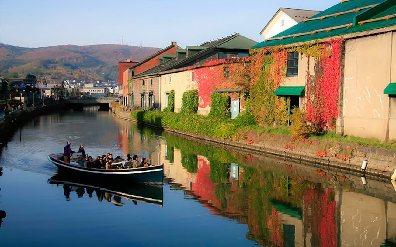 Boat tour on Otaru Canal with historic warehouses and autumn foliage.
