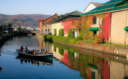 Boat tour on Otaru Canal with historic warehouses and autumn foliage.