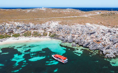 Red tour boat in turquoise water near rocky coastline.