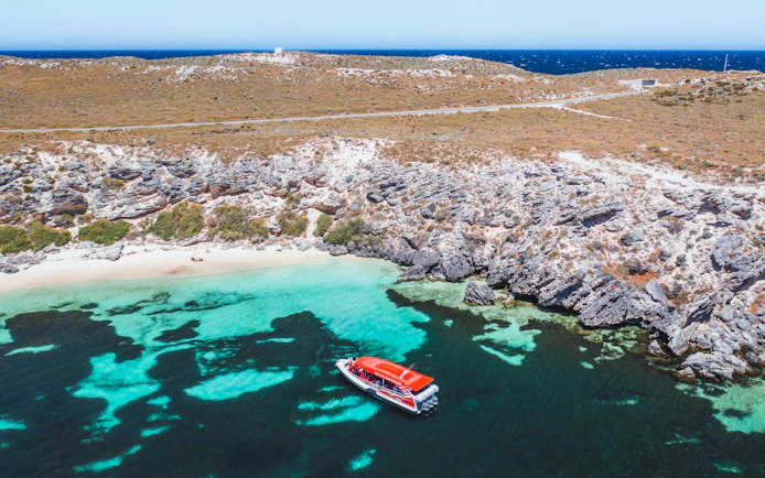 Red tour boat in turquoise water near rocky coastline.
