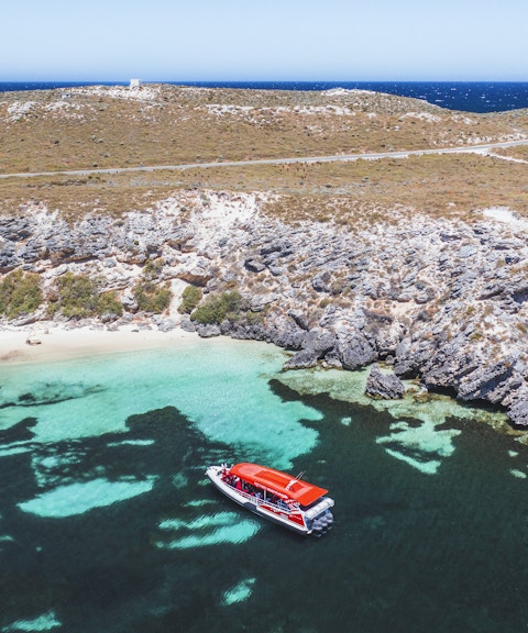 Red tour boat in turquoise water near rocky coastline.