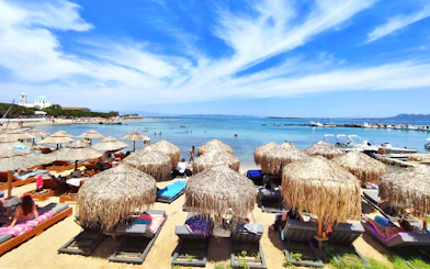Sun loungers and straw umbrellas on Skala beach, Agistri island, Greece, with clear blue sea.