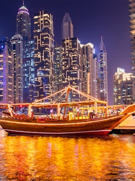 Dubai Marina lit up at night with a traditional dhow cruise on the water.