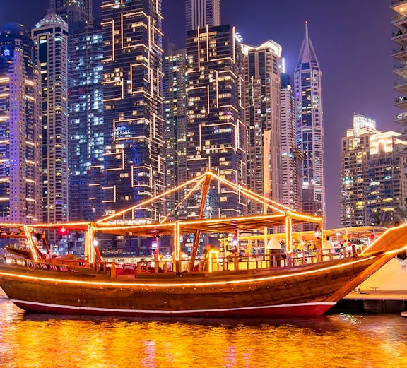 Dubai Marina lit up at night with a traditional dhow cruise on the water.