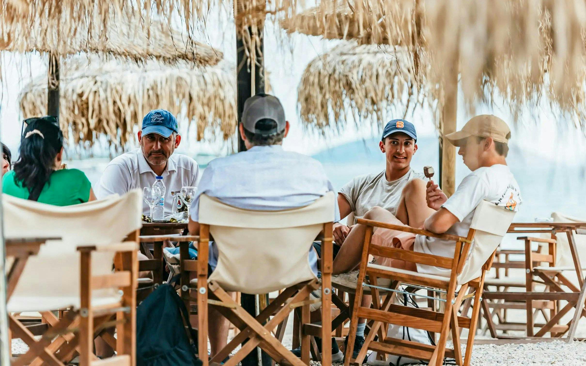 Group relaxing under straw umbrellas at a beachside cafe during Temple of Poseidon tour.