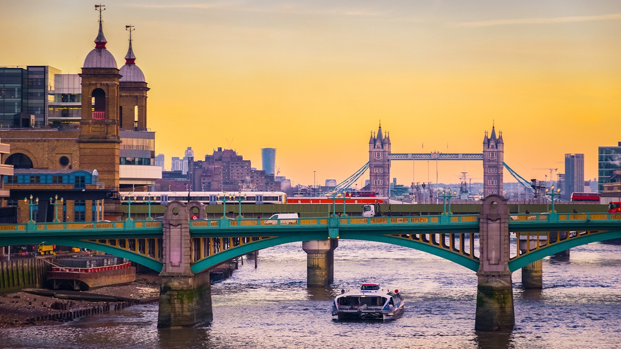 London cityscape with Tower Bridge and a boat on the Thames at sunset.