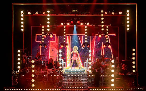 Performer on stage during TINA: The Tina Turner Musical with vibrant lighting and band.
