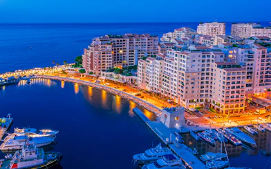 Monaco harbor at night with illuminated buildings and yachts.