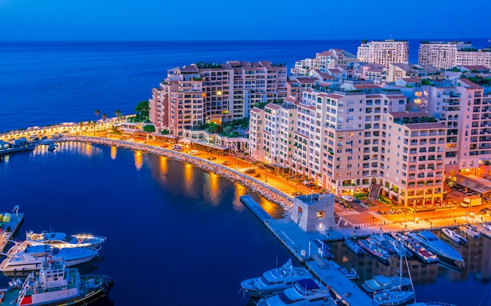 Monaco harbor at night with illuminated buildings and yachts.