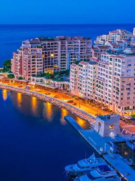 Monaco harbor at night with illuminated buildings and yachts.