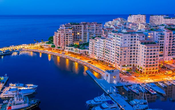 Monaco harbor at night with illuminated buildings and yachts.