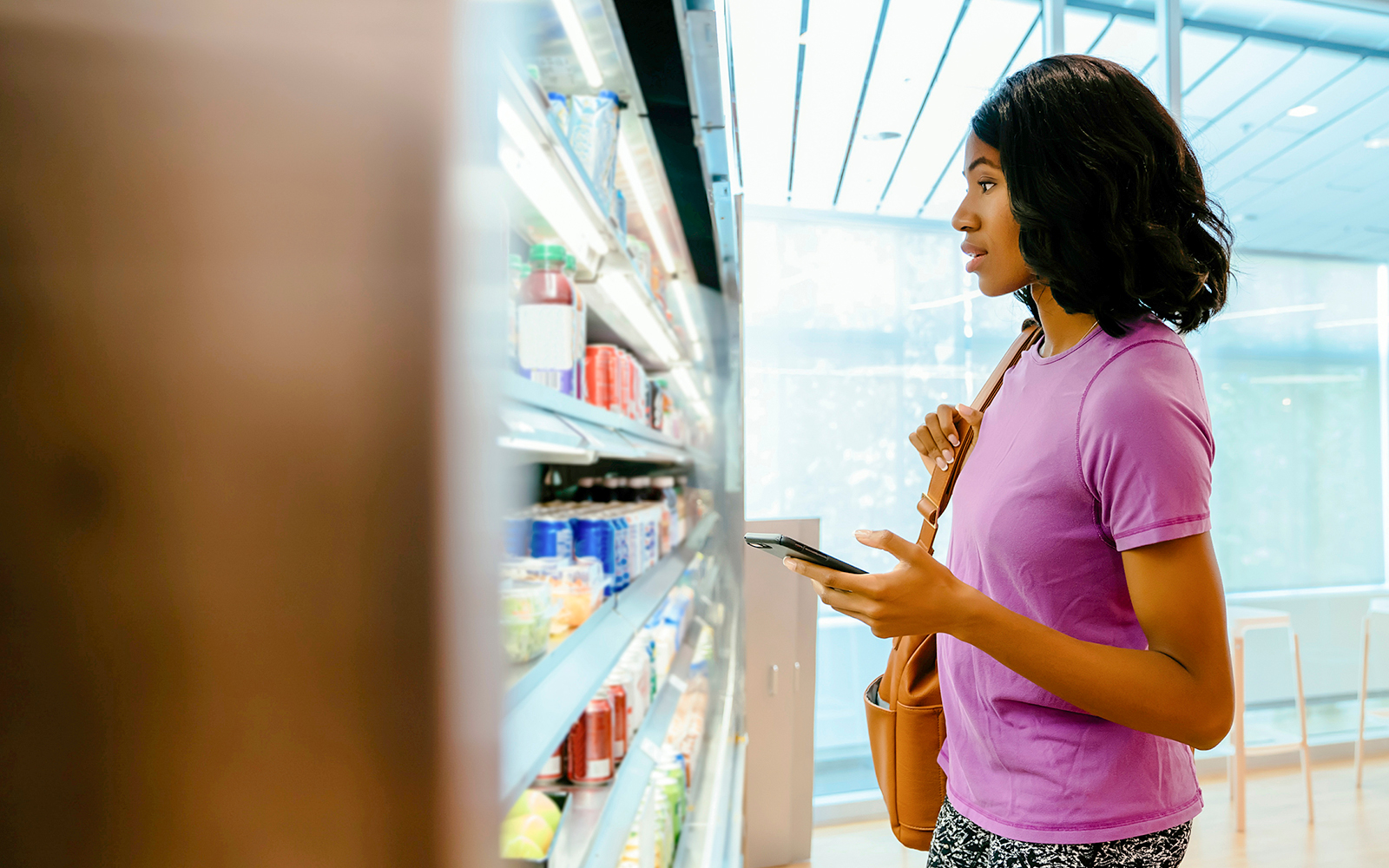 Woman shopping in a store aisle, holding a phone and a bag.