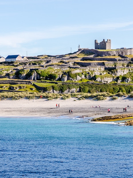 Inisheer Island beach with stone walls and castle ruins, Ireland.