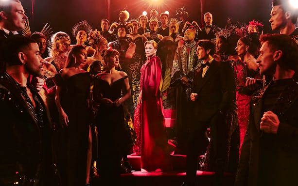 Cast of "The Devil Wears Prada" production in elaborate costumes on stage.