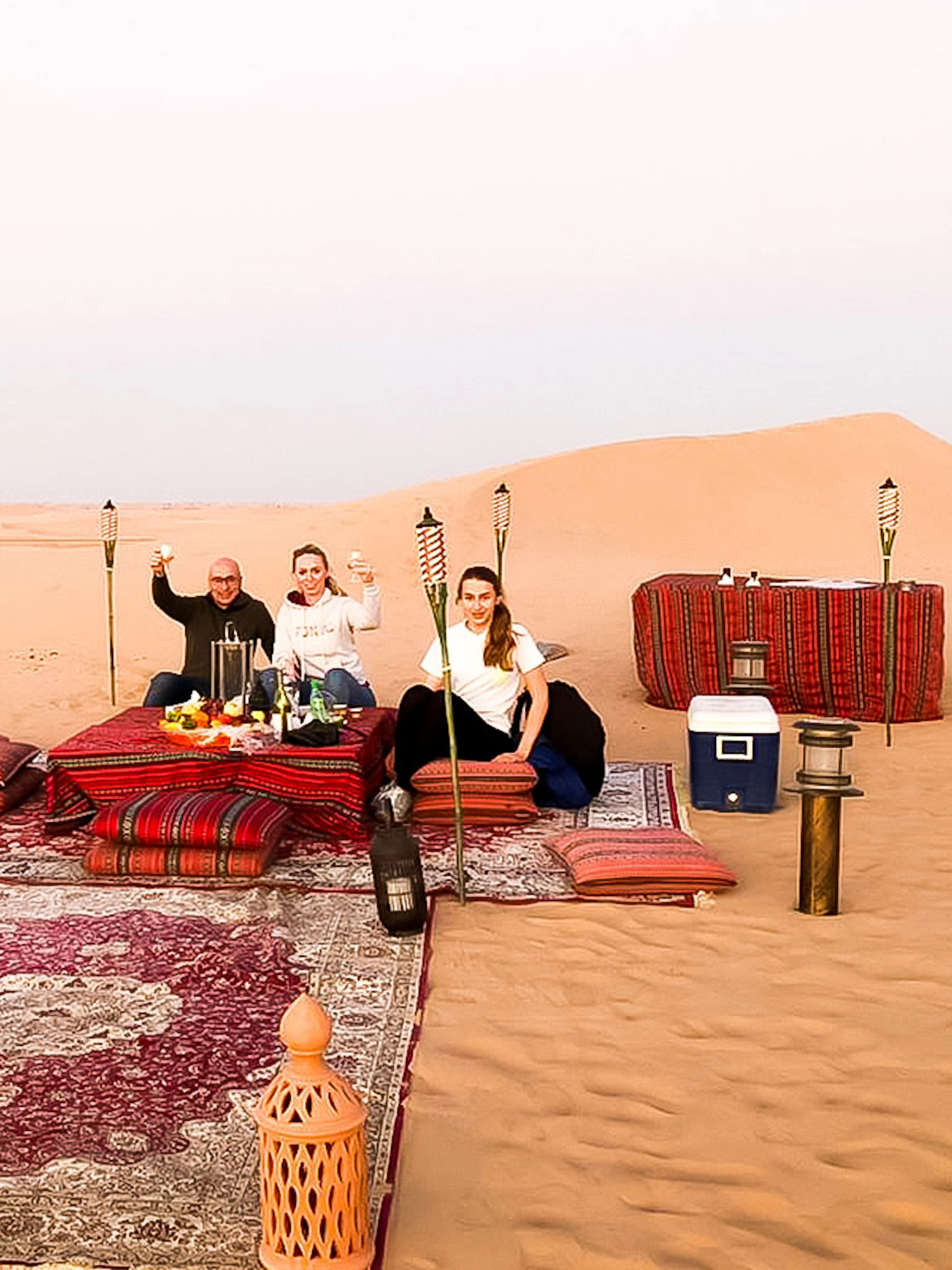Desert dinner setup with guests enjoying a meal on rugs surrounded by torches in Abu Dhabi dunes.