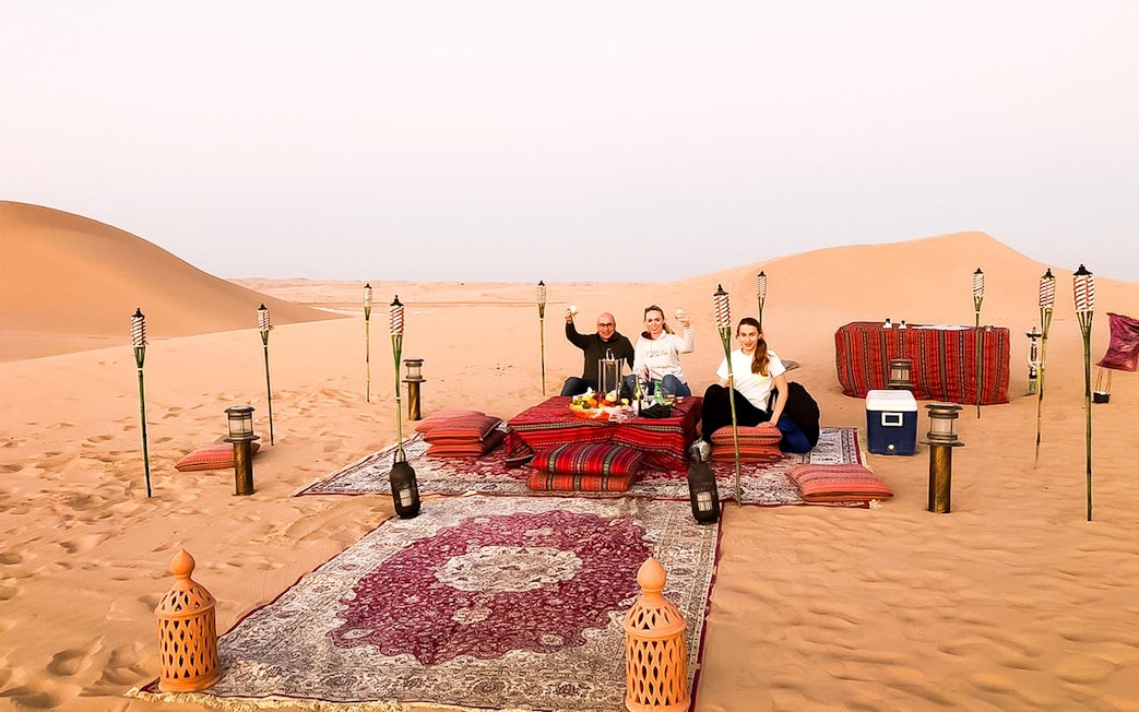 Desert dinner setup with guests enjoying a meal on rugs surrounded by torches in Abu Dhabi dunes.