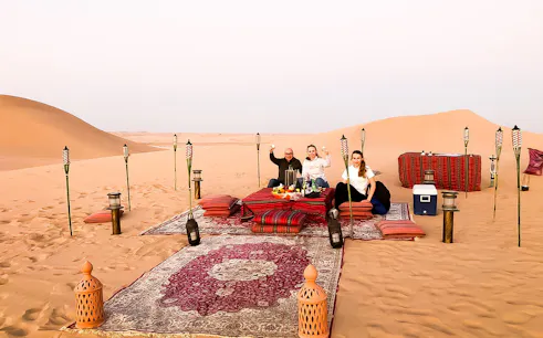 Desert dinner setup with guests enjoying a meal on rugs surrounded by torches in Abu Dhabi dunes.