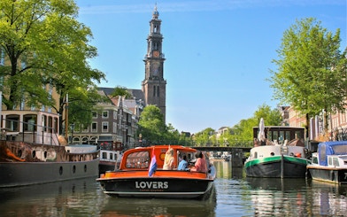 Canal cruise boat on Amsterdam canal with Westerkerk tower in the background.