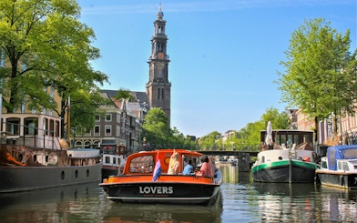 Canal cruise boat on Amsterdam canal with Westerkerk tower in the background.