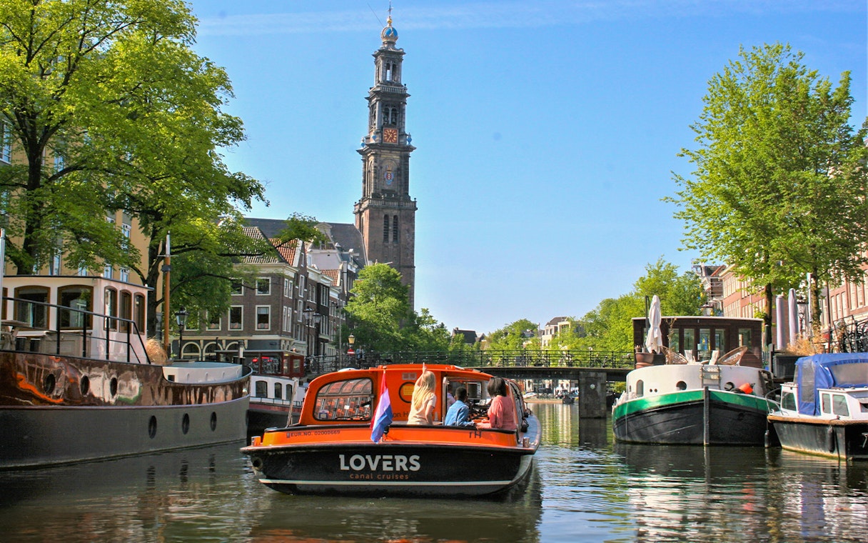 Canal cruise boat on Amsterdam canal with Westerkerk tower in the background.
