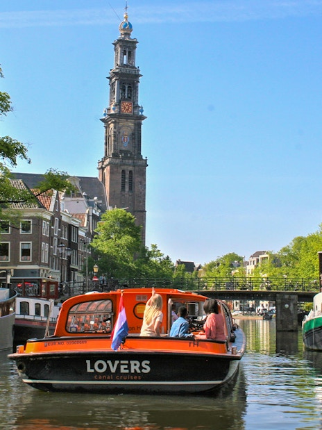 Canal cruise boat on Amsterdam canal with Westerkerk tower in the background.