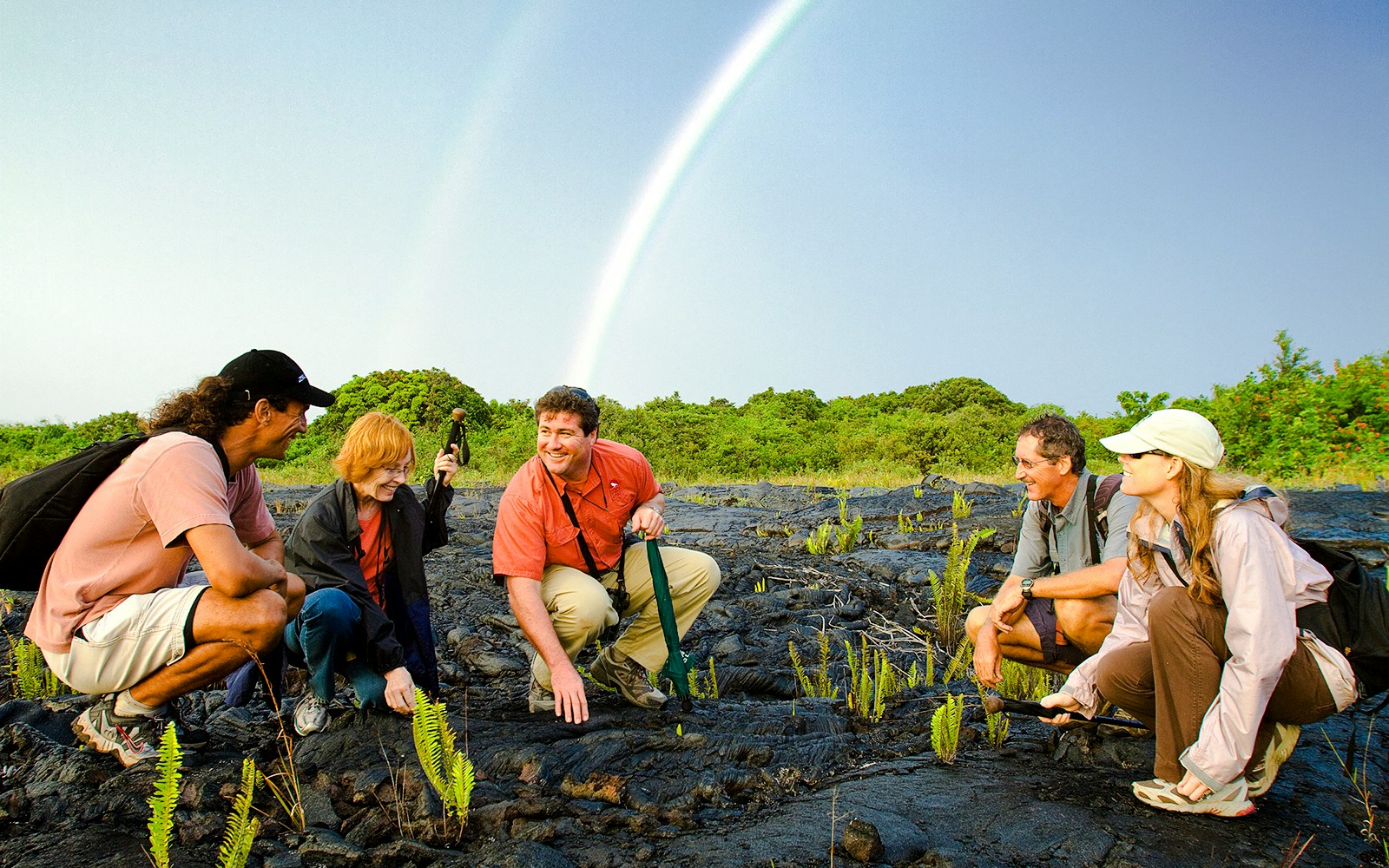Guests exploring volcanic terrain under a rainbow on Hawaii adventure tour.