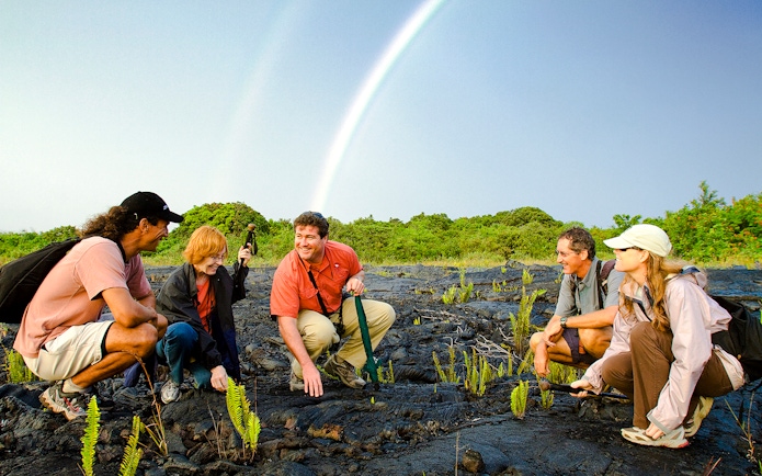 Guests exploring volcanic terrain under a rainbow on Hawaii adventure tour.