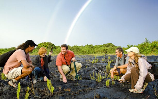 Guests exploring volcanic terrain under a rainbow on Hawaii adventure tour.