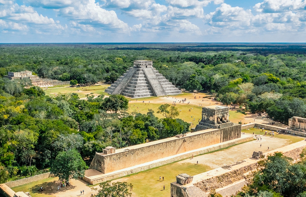 Aerial view of Chichen Itza with El Castillo pyramid surrounded by lush greenery.