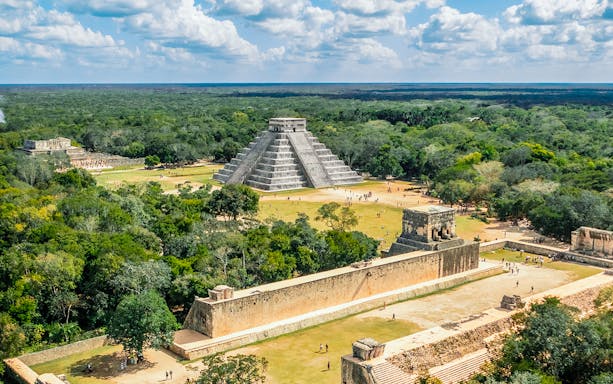 Aerial view of Chichen Itza with El Castillo pyramid surrounded by lush greenery.