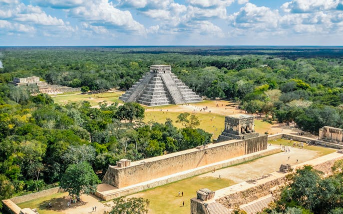 Aerial view of Chichen Itza with El Castillo pyramid surrounded by lush greenery.