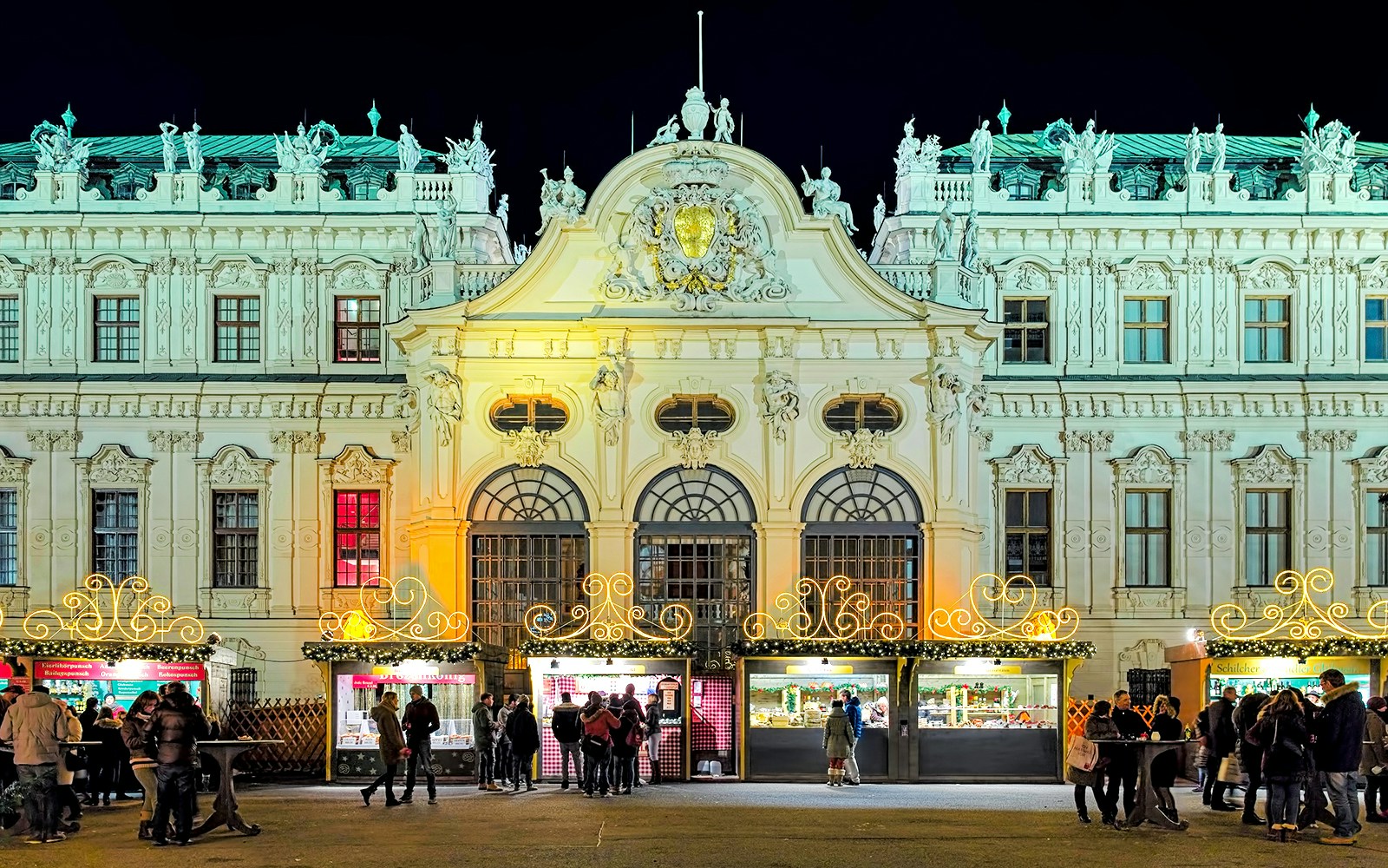 Christmas market stalls in front of the illuminated Upper Belvedere Palace, Vienna, Austria.