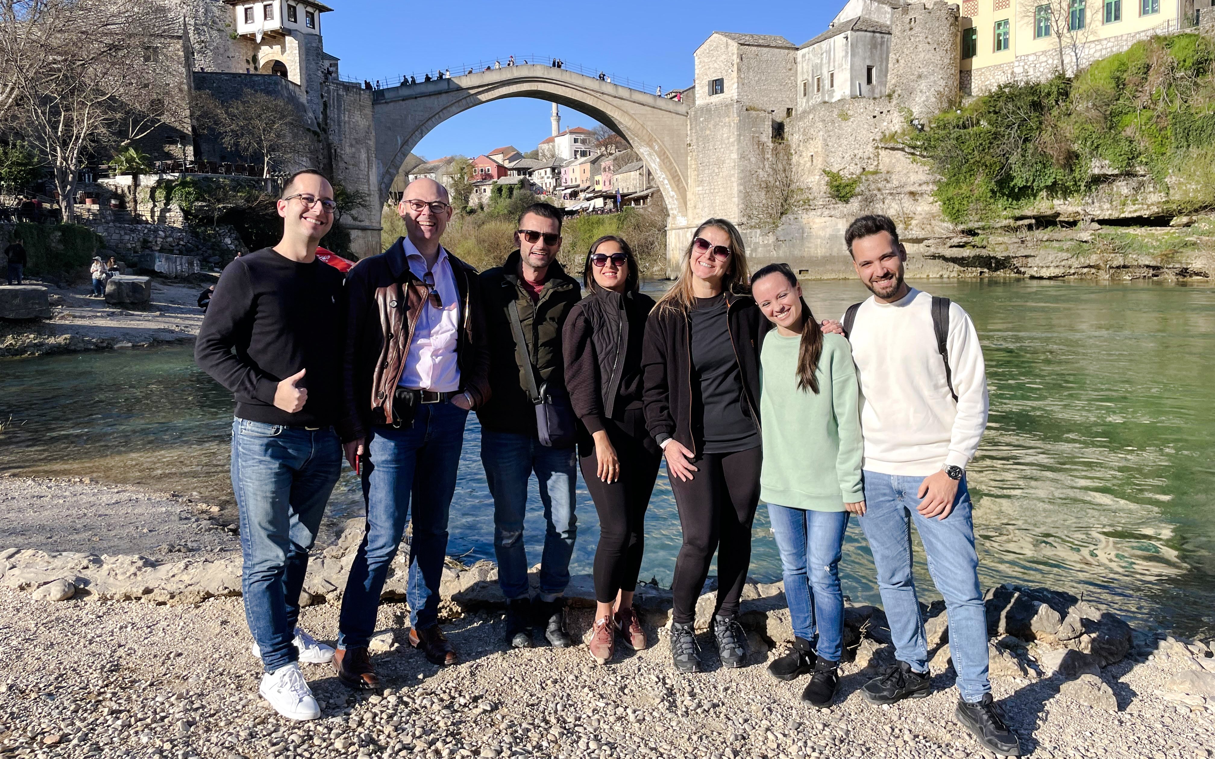 Group of tourists by the Neretva River with Mostar Bridge in Bosnia in the background.